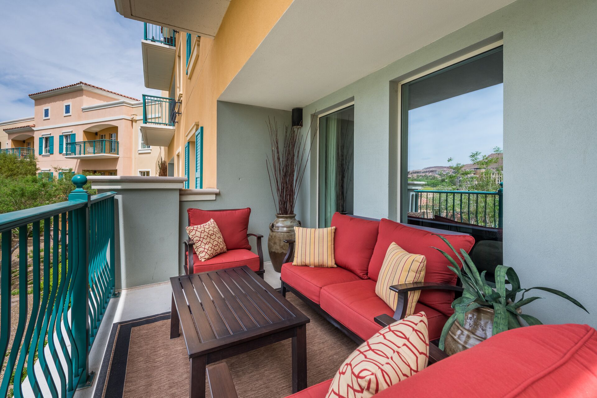 A balcony with a red sofa, a wooden table, and a potted plant.