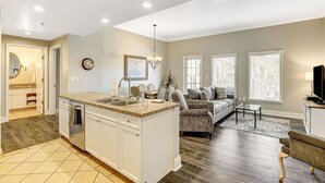 A modern kitchen with a central island, a dining area with a sofa and chairs, and a living room with a TV and a lamp.