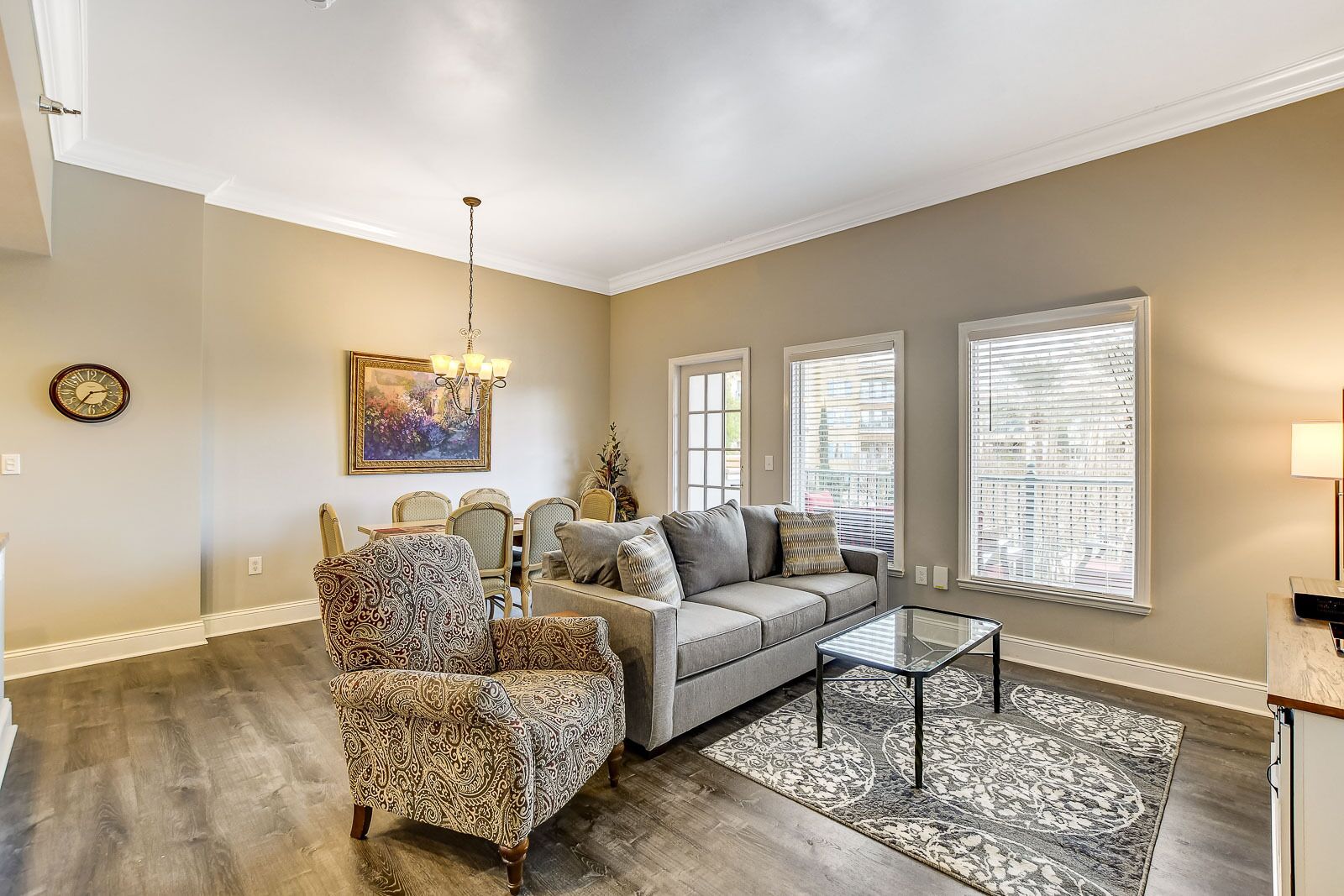 A living room with a sofa, armchair, dining table, and chandelier.