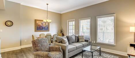 A living room with a sofa, armchair, dining table, and chandelier.