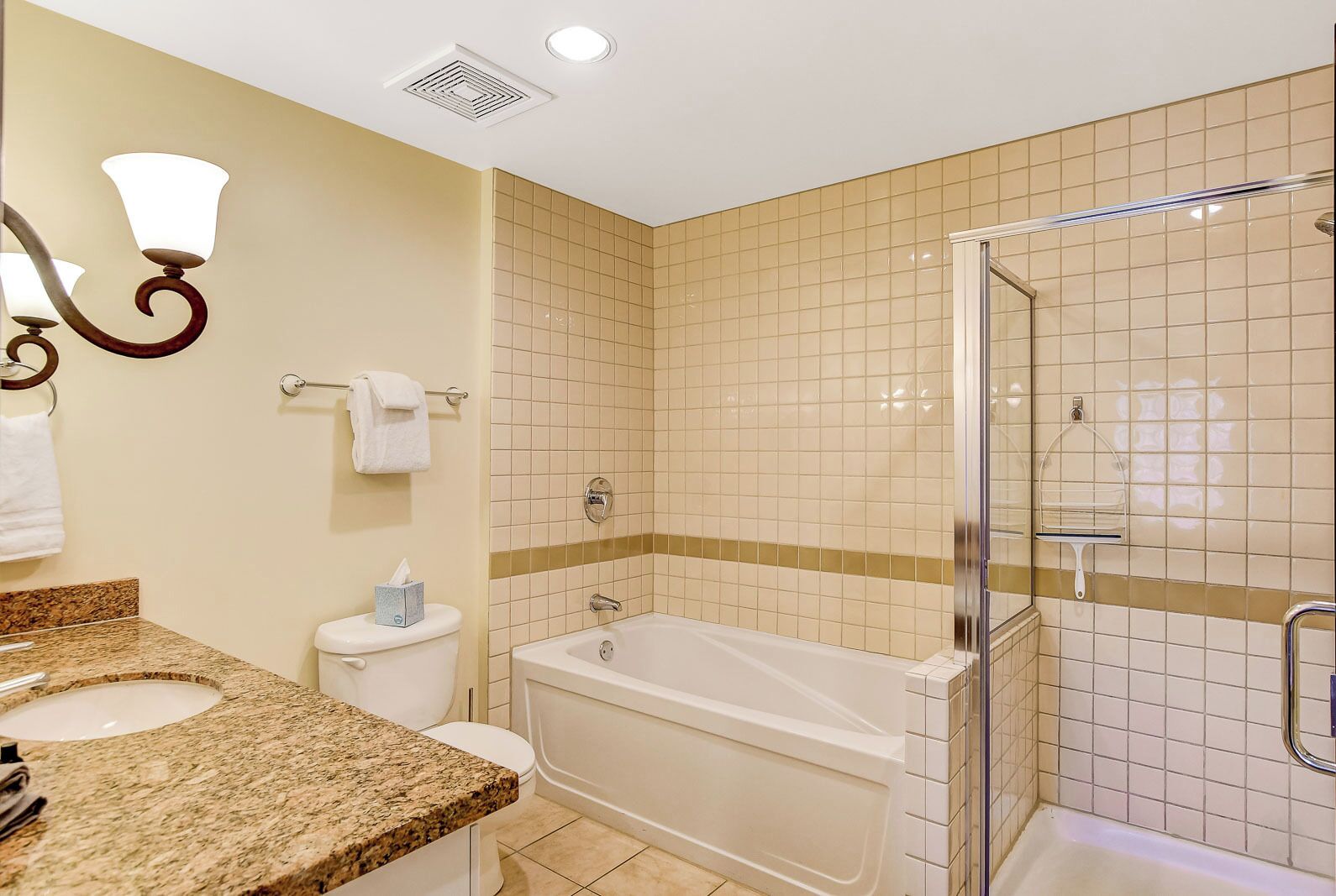 A bathroom with a granite countertop sink, a white toilet, a bathtub, and a glass shower enclosure.