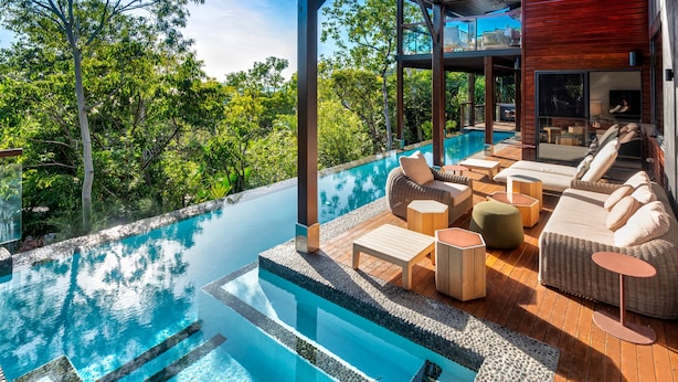An infinity pool with a wooden deck, outdoor furniture, and lush greenery in the background. - Point Blue, Beautiful House on Hamilton Island (Hamilton Island)
