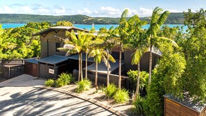 A modern beach house with a covered patio, surrounded by lush greenery and palm trees, overlooking a clear blue sea. - Point Blue, Beautiful House on Hamilton Island (Hamilton Island)