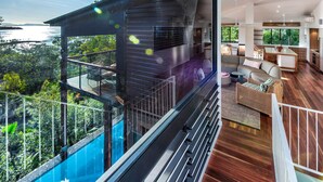 A modern interior with a large glass balcony overlooking a body of water, wooden flooring, and a cozy seating area. - Point Blue, Beautiful House on Hamilton Island (Hamilton Island)