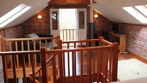 An attic bedroom with skylights, a wooden staircase, and a fireplace. - Historic brick stables (Otaki)
