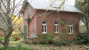 A small brick house with a gabled roof, surrounded by trees and a garden. - Historic brick stables (Otaki)
