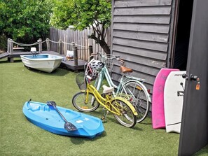 A backyard with a small boat, a bicycle, and a surfboard.