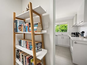 Een moderne keuken met witte kastjes, een houten boekenkast vol boeken en een raam met uitzicht op groen.