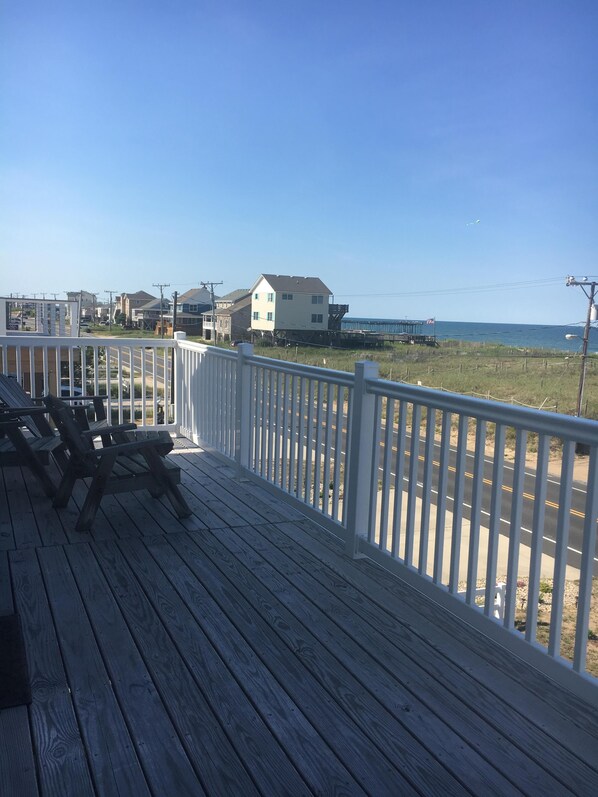 Relax on the deck overlooking the serene beach with comfortable seating and a view of the surrounding residential area.