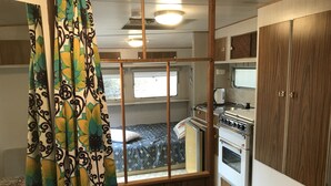 Ein kompaktes Wohnmobil-Interieur mit einer Küchenzeile, einem Bett und einem Fenster mit Vorhängen.