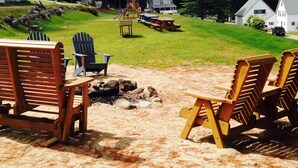 A beach setting with wooden Adirondack chairs, a picnic table, and a wooden play structure.