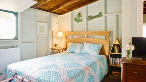 A bedroom with a wooden headboard, a bed with patterned bedding, a bedside table with a lamp, a bookshelf, and a television on a dresser.