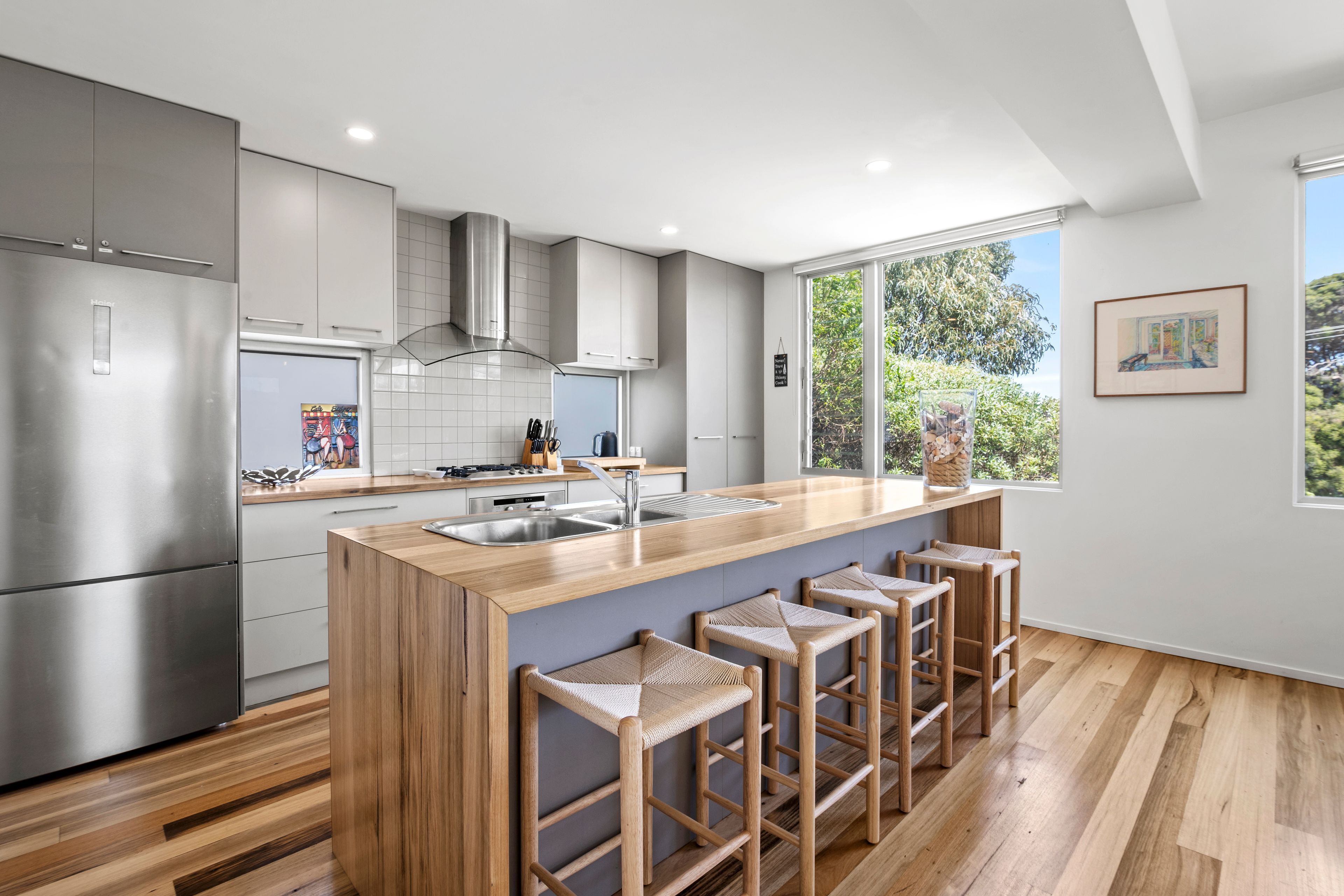 A modern kitchen with a central island, bar stools, and a large window.