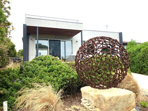 Un bâtiment moderne doté d’une grande porte en verre, d’une sculpture métallique et d’un espace vert bien entretenu.