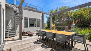 Um pátio moderno ao ar livre com deck de madeira, mesa de jantar com cadeiras e área para churrasqueira integrada.