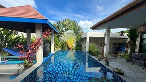 En swimmingpool med blå mosaikplattor, omgiven av krukväxter och en palm.