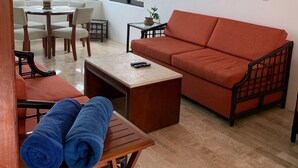 Una sala de estar con sofá, mesa de centro, mesa de comedor con sillas y ventilador de techo.