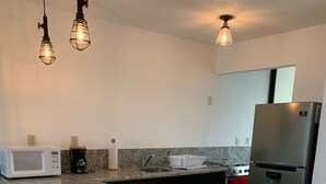 Una cocina moderna con encimeras de granito, microondas integrado, cafetera, lavamanos, estufa y refrigerador de acero inoxidable.