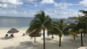 Una playa con palmeras, sillas de descanso y una sombrilla de paja.