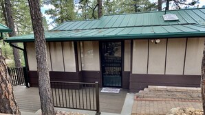 A building with a green roof, a wooden door, and a small porch area. - Cozy Cabin: Deck, Hot Tub, Views & Starry Nights (Prescott)