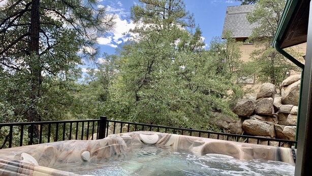 A hot tub with a marble design, surrounded by a black metal fence, set against a backdrop of trees and a stone wall. - Cozy Cabin: Deck, Hot Tub, Views & Starry Nights (Prescott)