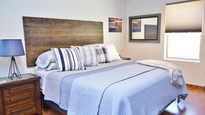 A bedroom with a wooden headboard, a bed with striped bedding, a nightstand with drawers, and a window with blinds. - Cozy Cabin: Deck, Hot Tub, Views & Starry Nights (Prescott)