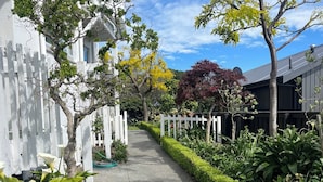 Un sentier bordé de clôtures blanches et d’une végétation luxuriante, qui mène à un bâtiment doté de grandes fenêtres.