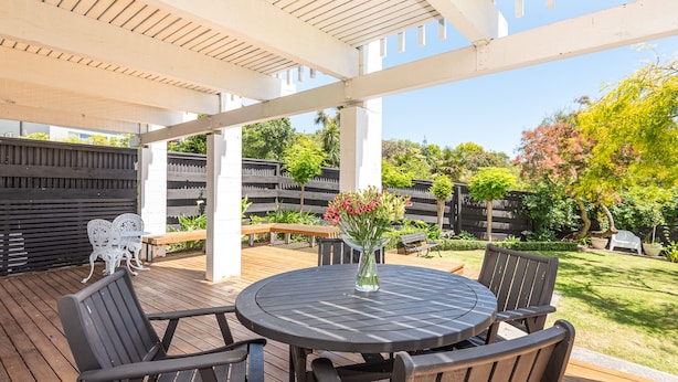 Une terrasse extérieure avec une table ronde et des chaises, entourée d’une plateforme en bois et d’une pergola blanche.