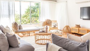Ein helles Wohnzimmer mit großem Fenster, Korbmöbeln und einem Flachbildfernseher.