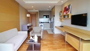 Un soggiorno moderno con un divano, un tavolino e una TV. Si nota una cucina sullo sfondo, con lavatrice e frigorifero.