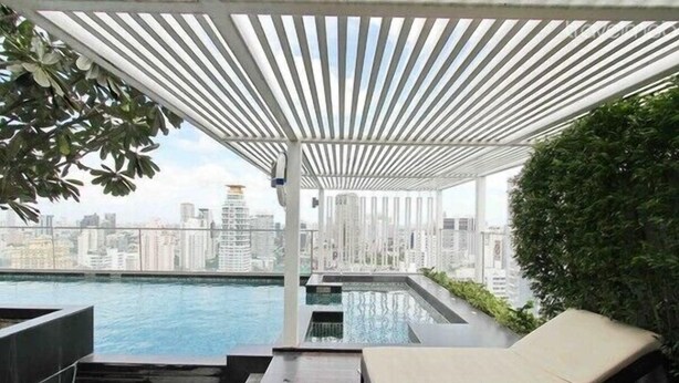 Una piscina a sfioro sul tetto con vista sulla città, sedie a sdraio e una struttura a pergola.