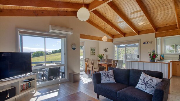 Un salón amplio con un televisor grande, vigas de madera en el techo y vistas al exterior.