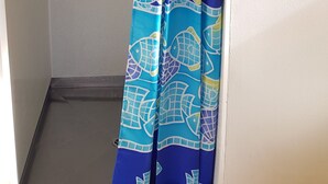 Un baño con cortina de ducha estampada con un diseño de peces azules y verdes, un tendedero de toallas metálico y una pared blanca.
