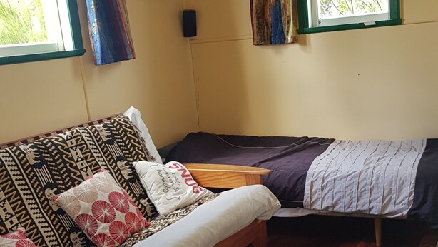Una habitación con piso de madera, un sofá con cojines estampados, una pequeña mesa de madera y una cama con una colcha blanca.