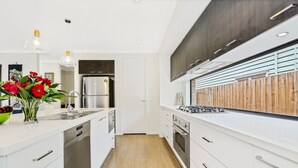 A modern kitchen with white cabinetry, stainless steel appliances, and a wooden floor.