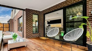 A modern patio with wooden flooring, white wicker chairs, and a glass table.