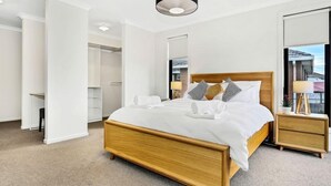 A modern hotel room with a wooden bed, white linens, a bedside table with a lamp, and a view of the outside.