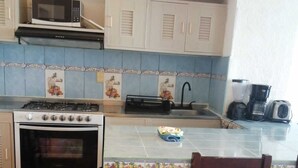 A compact kitchen with a stove, oven, microwave, and a small island with a chair.
