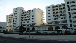 A multi-story hotel with balconies and a parking area in front.