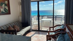 A room with a sofa, a dining table, and a view of the ocean through large glass doors.