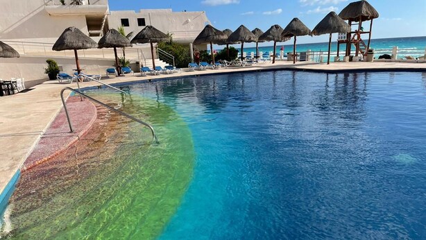 A pool with clear water, lounge chairs, and thatched umbrellas.
