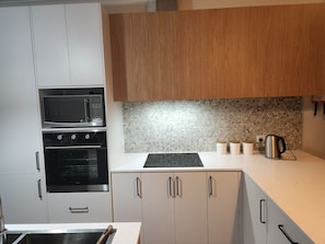 Eine moderne Küche mit weißen und hölzernen Schränken, einer Mikrowelle, einem Backofen und einer gefliesten Spritzschutzwand.