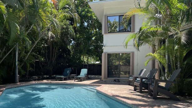 Una piscina con borde de azulejos, rodeada de sillas de descanso y palmeras.