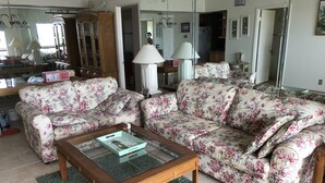 Uma sala de estar com sofás estampados com florais, uma mesa de centro de vidro e um tapete verde.