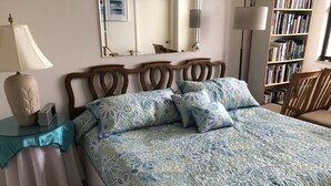 Quarto com uma cama, mesa de cabeceira com abajur, espelho e estante de livros.