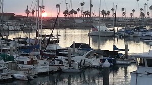 A marina with various boats docked, a sunset in the background, and palm trees lining the shore. - Romantic Getaway for 2 in Cottage in complex right on the beach (Oceanside)