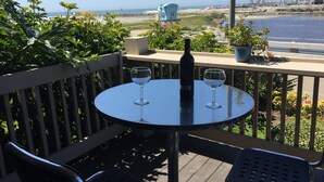 A round table with a bottle and two wine glasses on a balcony overlooking a beach. - Romantic Getaway for 2 in Cottage in complex right on the beach (Oceanside)