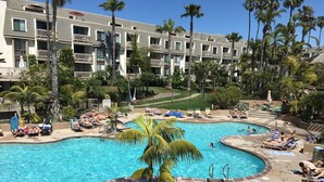A resort pool area with multiple lounge chairs, palm trees, and a large building in the background. - Romantic Getaway for 2 in Cottage in complex right on the beach (Oceanside)