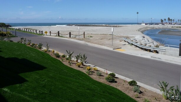 A coastal road with a grassy median, palm trees, and a clear view of the beach and ocean. - Romantic Getaway for 2 in Cottage in complex right on the beach (Oceanside)