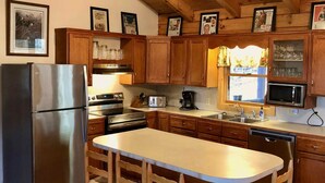 Una cocina con armarios de madera, un refrigerador de acero inoxidable, una isla central con taburetes y un ventilador de techo.
